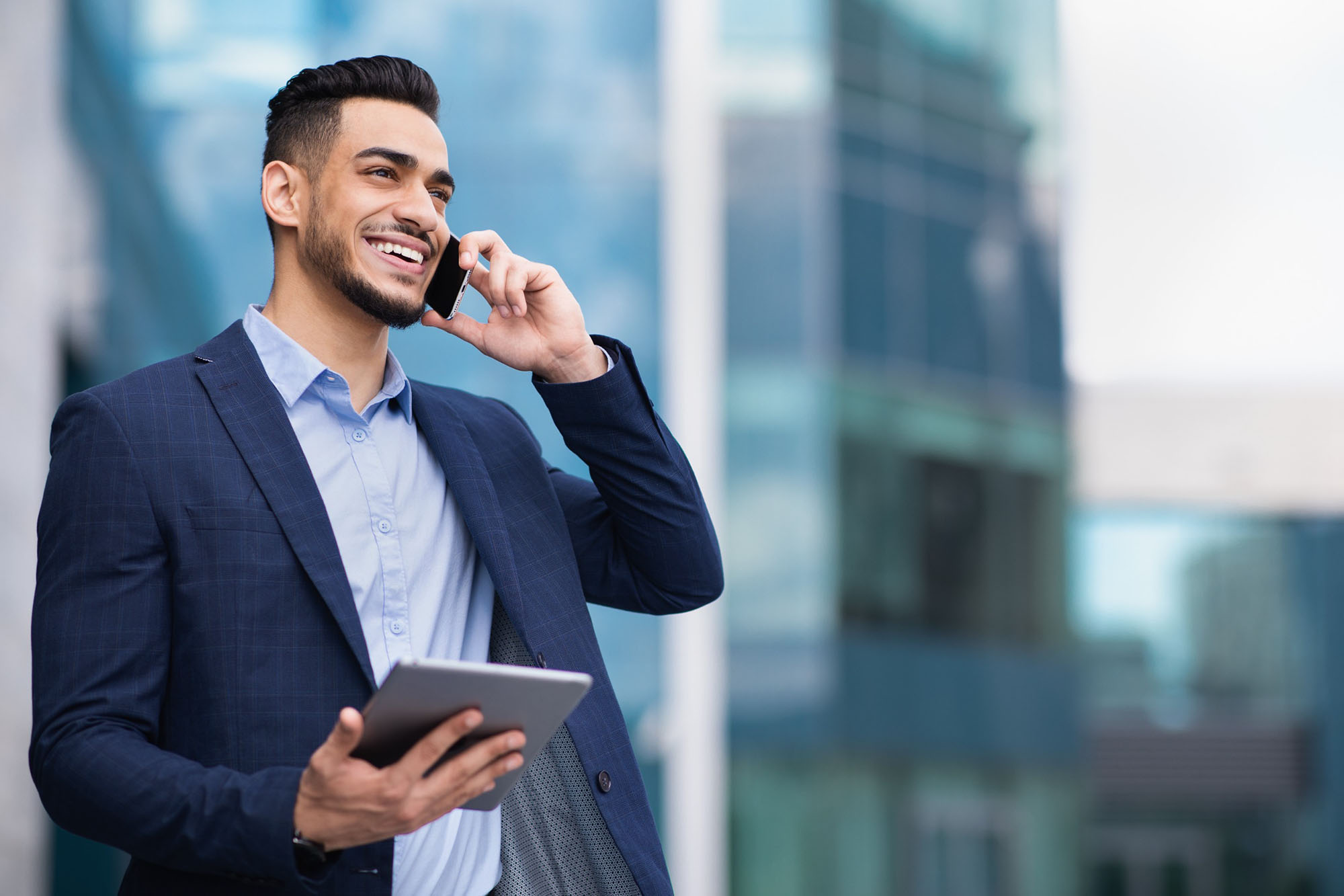 A man in a suit holding a mobile phone up to his ear and smiling